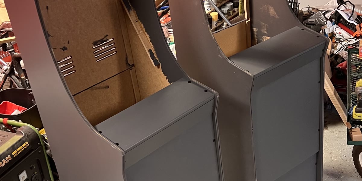 Two partially built arcade cabinets in gray primer standing in the garage, two weeks before the wedding