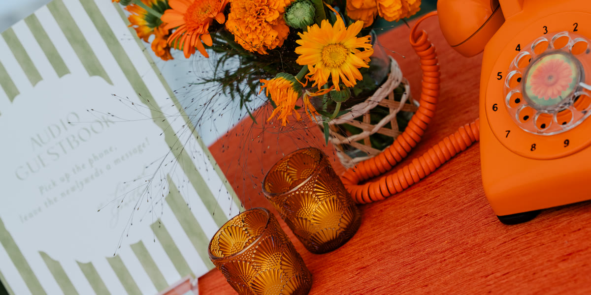 The audio guestbook table at an outdoor wedding, rotary phone, guestbook sign, candles, and marigolds
