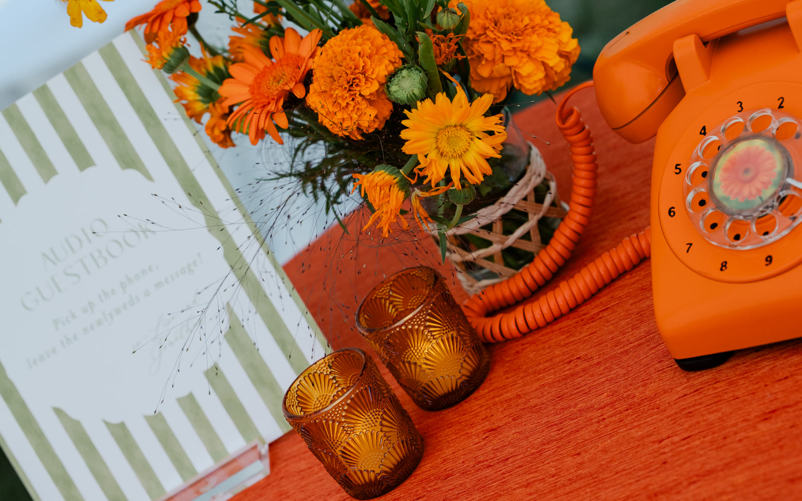 Audio guestbook table at an outdoor wedding — rotary phone, guestbook sign, candles, and marigolds
