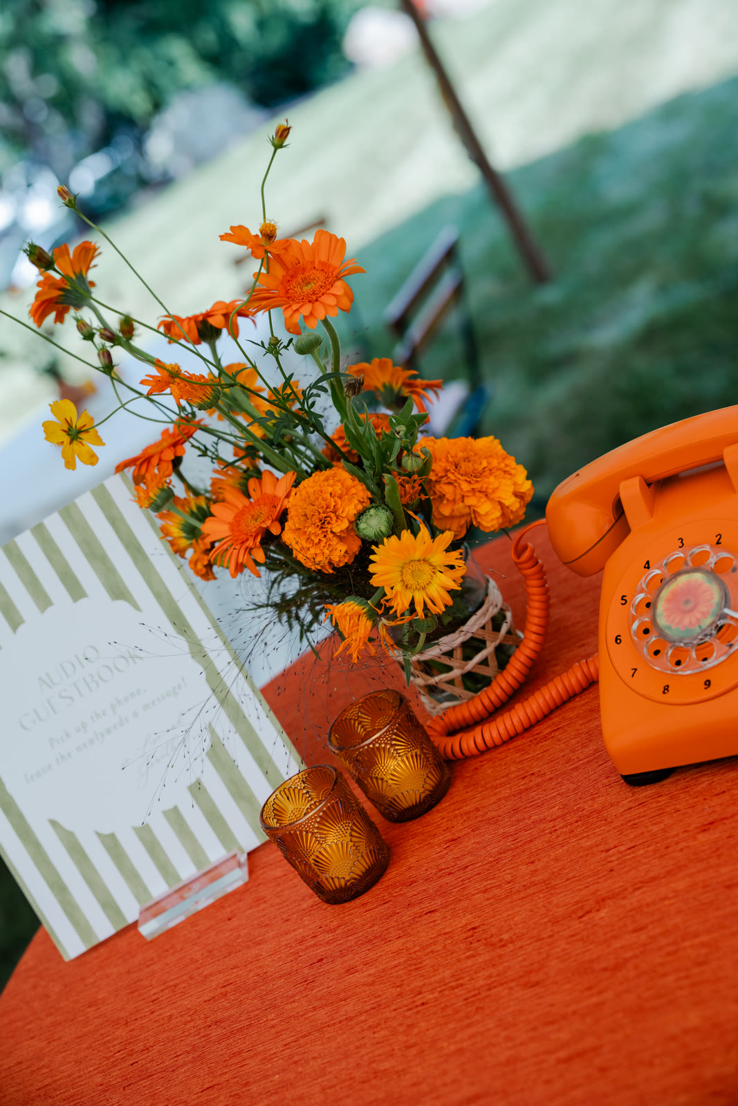 Audio guestbook table with a rotary phone, sign, and flowers at an outdoor wedding